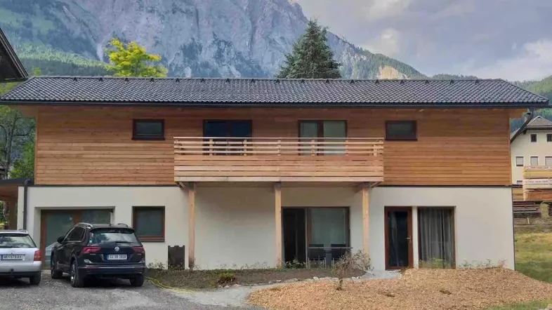 Modernes Gebäude mit Holzfassade, Balkon und beeindruckendem Bergblick in alpiner Umgebung.