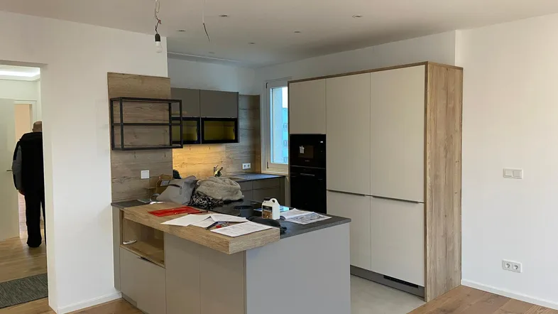 Moderne Küche mit Kücheninsel, integrierten Geräten und Holzboden in einem offenen Wohnbereich.