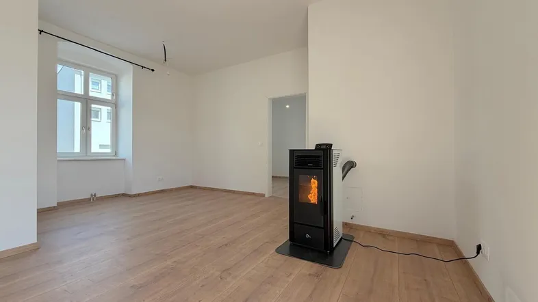 Helles, leeres Zimmer mit Holzboden und einem modernen Pelletofen als Wärmequelle.