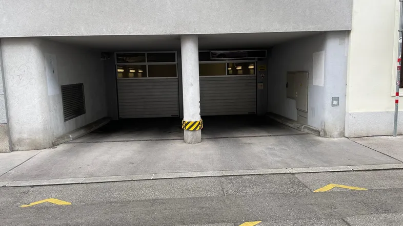 Eingang zu einer Tiefgarage mit zwei Rolltoren und gelben Markierungen auf dem Boden.