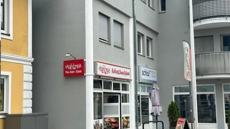 Graues Mehrfamilienhaus mit Geschäftsräumen im Erdgeschoss und Wohnungen darüber, an einer Straße gelegen.