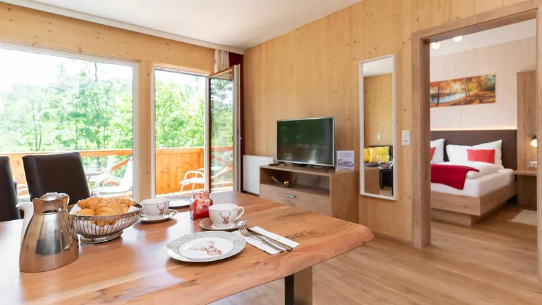 Helles Wohn- und Esszimmer mit Holzwänden, Balkonzugang und Blick ins Grüne.