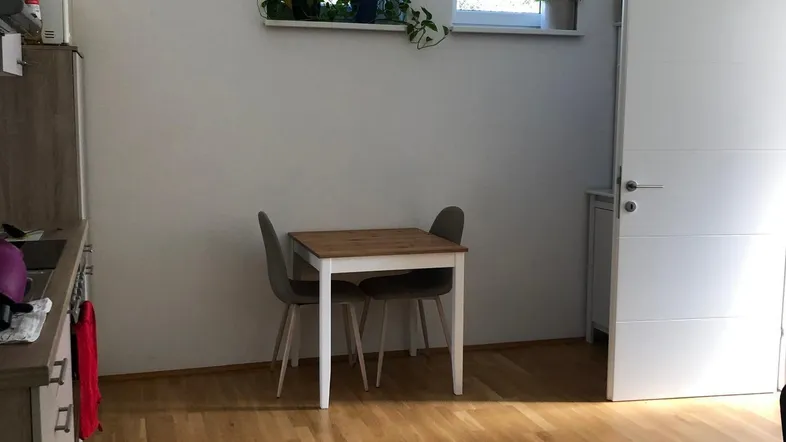 Helle Küche mit Holzboden, kleiner Essecke und Blick ins Grüne durch die Fenster.