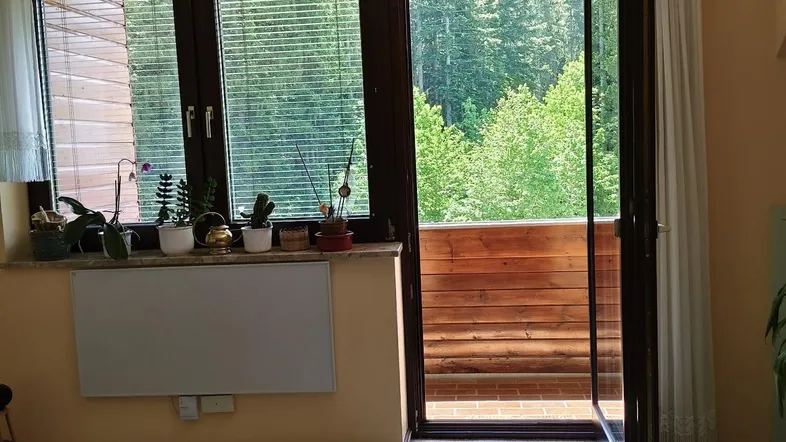Helles Zimmer mit Zugang zum Balkon und Blick ins Grüne, ausgestattet mit Jalousien.