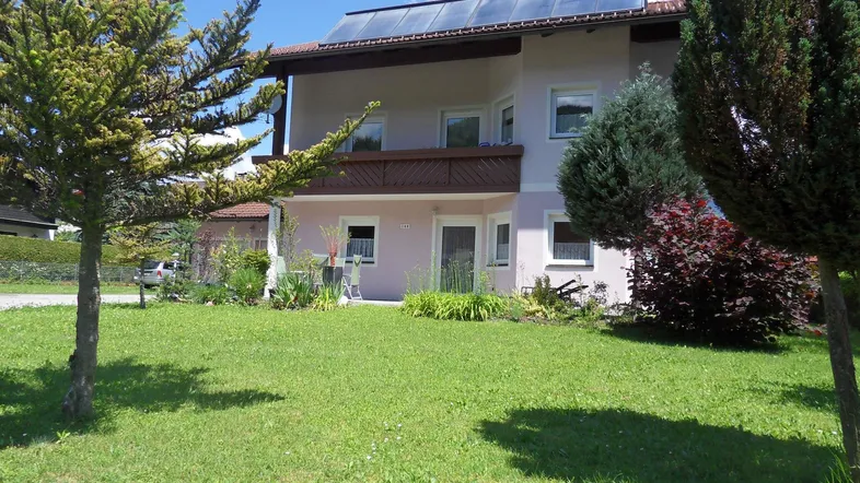 Einfamilienhaus mit gepflegtem Vorgarten, Balkon und Solarpaneelen auf dem Dach.