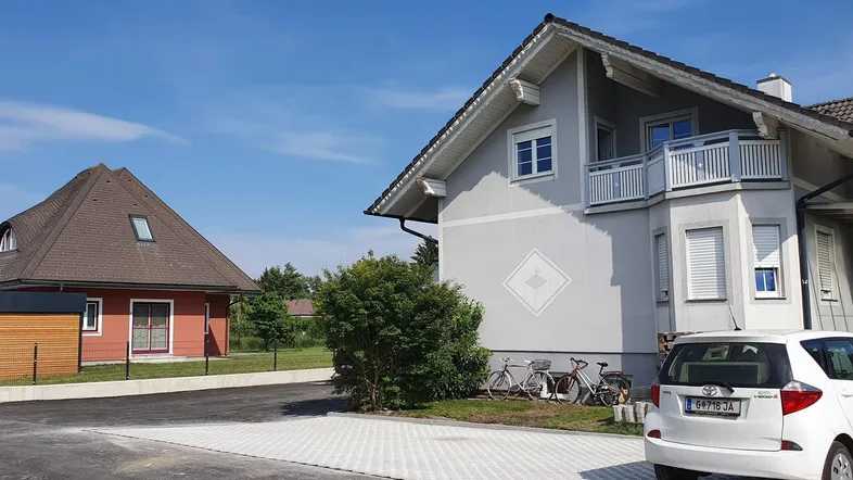 Zwei Wohnhäuser mit gepflasterter Einfahrt und einem geparkten Auto unter blauem Himmel.