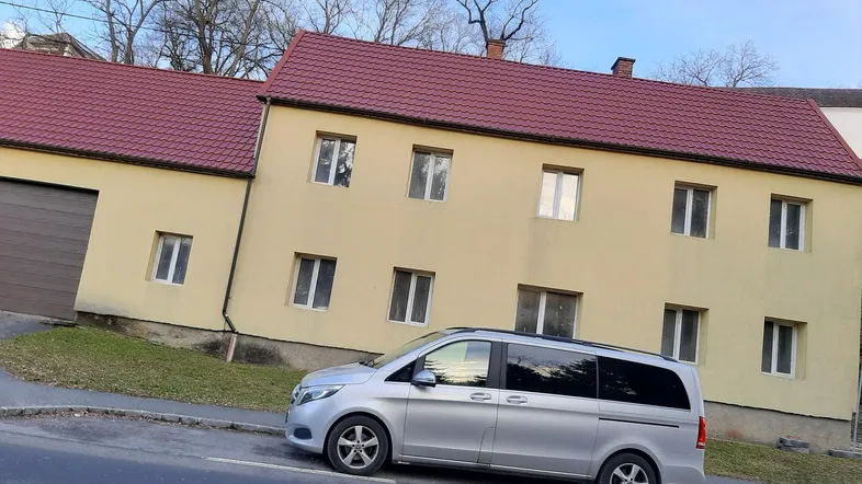 Gelbes Gebäude mit rotem Ziegeldach und einem geparkten Van auf der Straße davor.