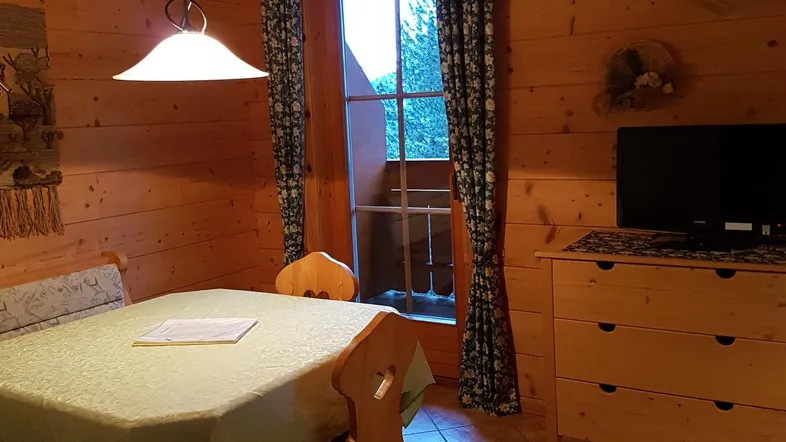 Rustikaler Essbereich mit Holzwänden, Fliesenboden und Blick ins Grüne durch das Fenster.