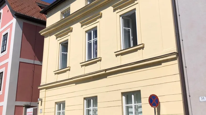 Historisches Gebäude mit heller Fassade und klassischen Fenstern in einer städtischen Umgebung.