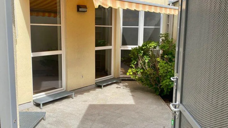 Gepflasterte Terrasse mit Markise und Zugang zu den Innenräumen, umgeben von Grün.