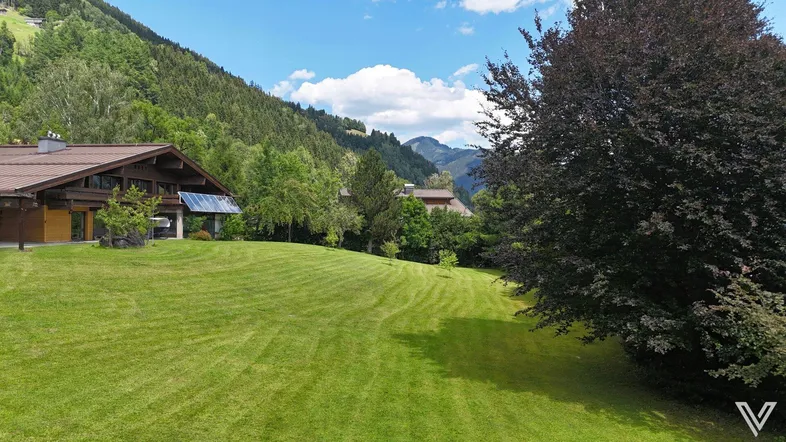 Weitläufiger grüner Garten mit gepflegtem Rasen, umgeben von Bäumen und mit Blick auf die Berge.