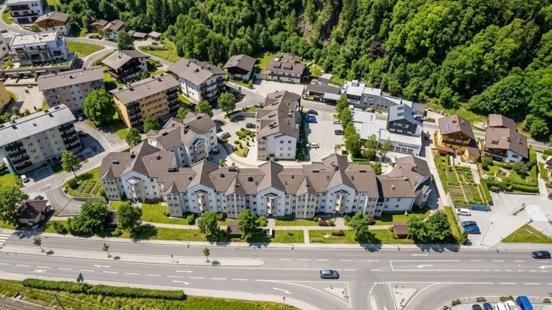 Luftaufnahme einer modernen Wohnanlage, eingebettet in eine grüne Landschaft mit umliegenden Bergen.