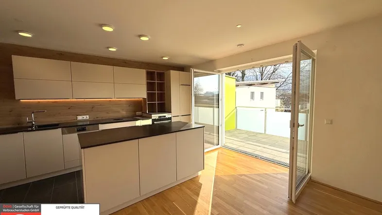 Moderne Küche mit Kücheninsel, Holzboden und Zugang zu einer sonnigen Terrasse.