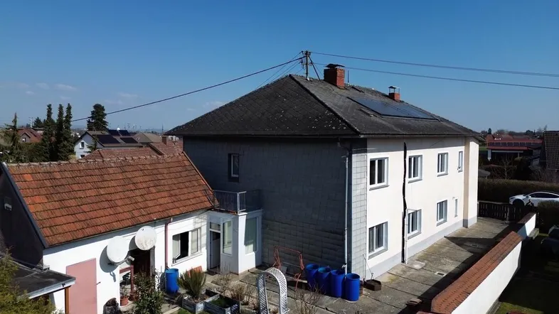 Blick auf das Wohnhaus mit angrenzendem Nebengebäude und einem kleinen Gartenbereich mit Schaukel.