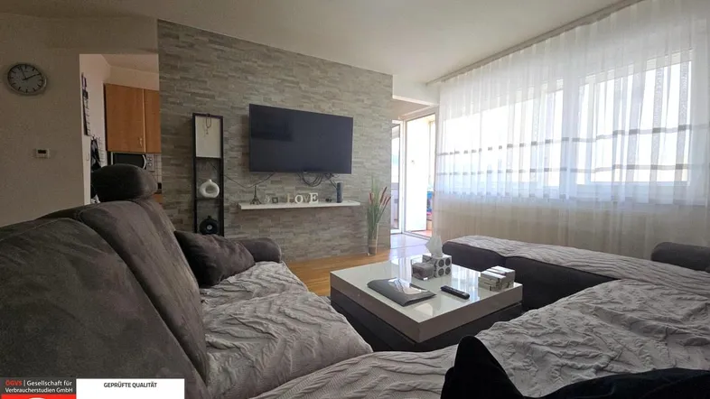 Gemütliches Wohnzimmer mit großem Sofa, modernem Couchtisch und einem Fernseher an einer Steinwand.