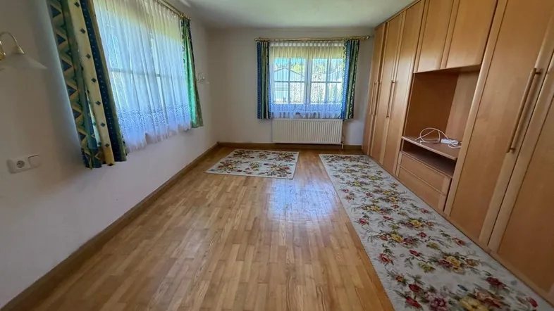 Helles Schlafzimmer mit Holzfußboden, Einbauschränken und zwei Fenstern für natürliches Licht.
