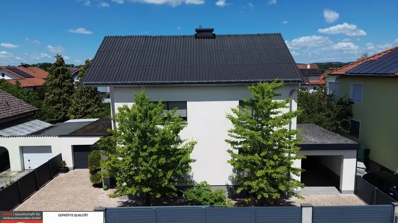 Modernes Einfamilienhaus mit Satteldach, Carport und gepflegtem Vorgarten unter blauem Himmel.