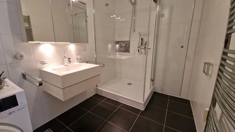 Modernes Badezimmer mit ebenerdiger Dusche, Waschbecken und Spiegelschrank, ausgestattet mit Waschmaschine.