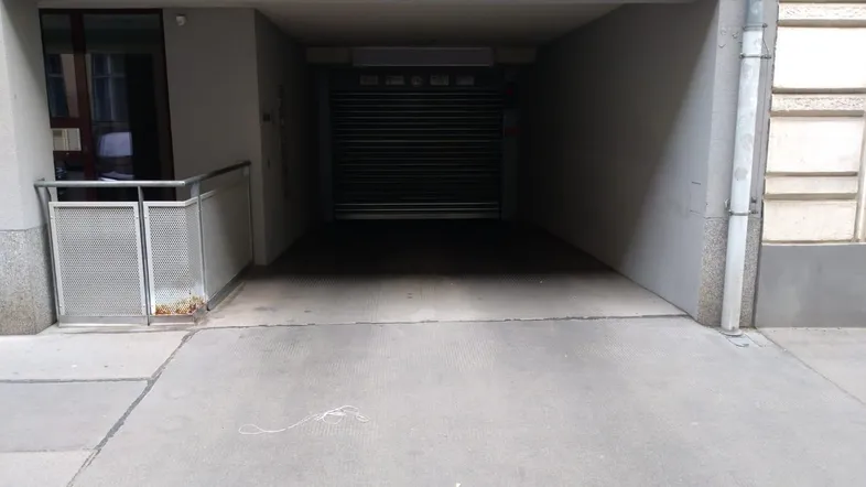 Einfahrt zu einer Tiefgarage mit geschlossenem Garagentor und Zugang zum Gebäude.