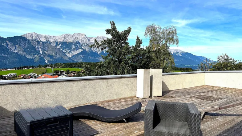 Große Dachterrasse mit Loungemöbeln und atemberaubendem Bergblick unter blauem Himmel.