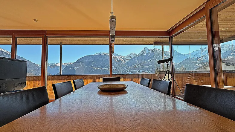 Geräumiger Essbereich mit großem Holztisch und raumhohen Fenstern, die einen atemberaubenden Bergblick bieten.