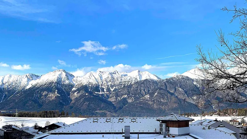 Panoramablick auf die schneebedeckten Berge über den Dächern der umliegenden Häuser unter blauem Himmel.