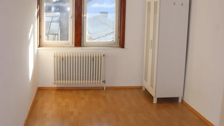 Helles Zimmer mit Laminatboden, Fenster und einem Heizkörper, ideal als Schlaf- oder Arbeitszimmer.