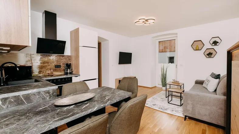 Heller offener Wohn-Essbereich mit moderner Küche, Holzboden und gemütlichem Sofa.