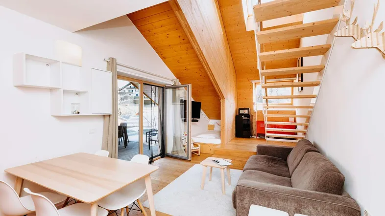 Helles Wohn- und Esszimmer mit Holzboden, offener Treppe und Zugang zur Terrasse.