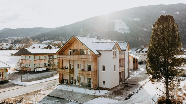 Modernes Mehrfamilienhaus in alpiner Umgebung mit Holzbalkonen und schneebedeckten Dächern.