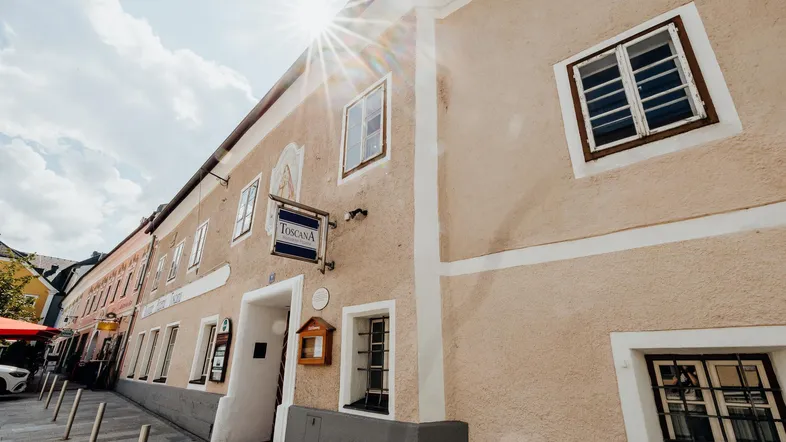 Historisches Gebäude mit traditioneller Fassade und Sonnenschein, das eine Pizzeria beherbergt.