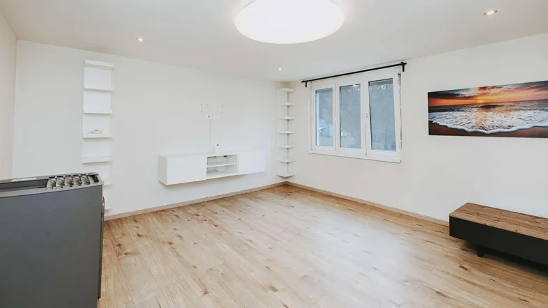 Geräumiges Wohnzimmer mit hellem Holzboden, weißen Wänden und moderner Wanddekoration.