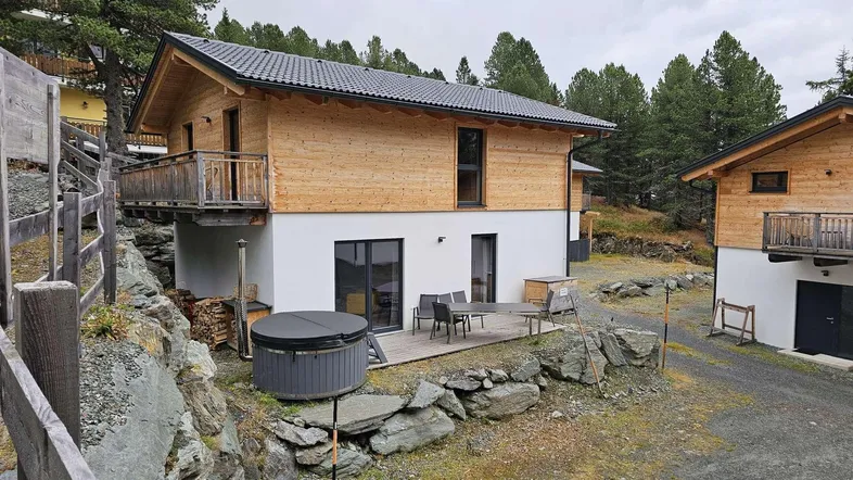 Modernes Chalet mit Holzfassade, Terrasse, Whirlpool und Blick auf die umliegende Natur.