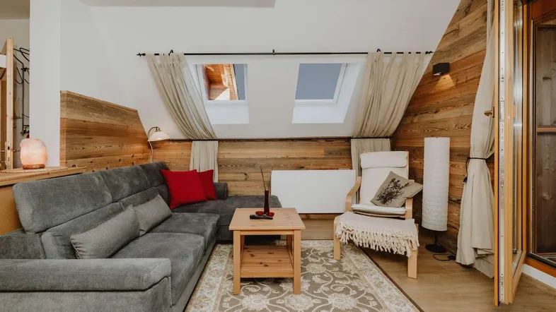 Gemütliches Wohnzimmer mit Dachschrägen, Holzwänden, Sofa und zwei Dachfenstern für viel Licht.