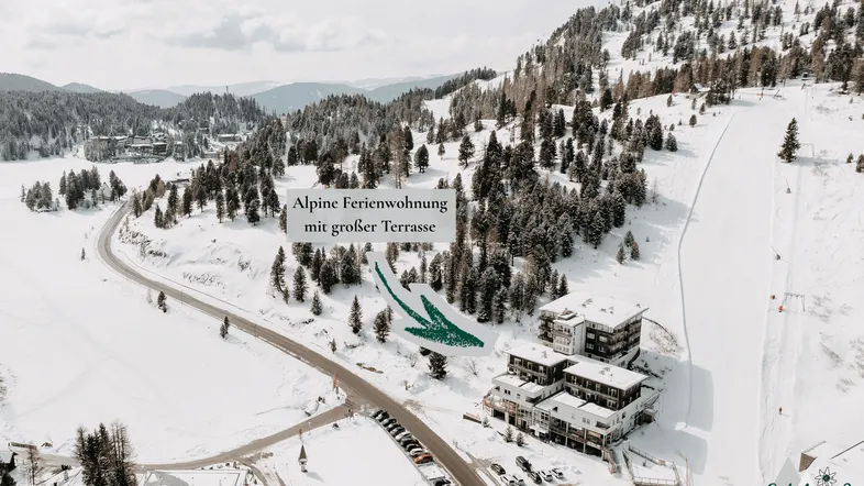 Luftaufnahme einer alpinen Ferienwohnung in verschneiter Berglandschaft mit Skigebiet.