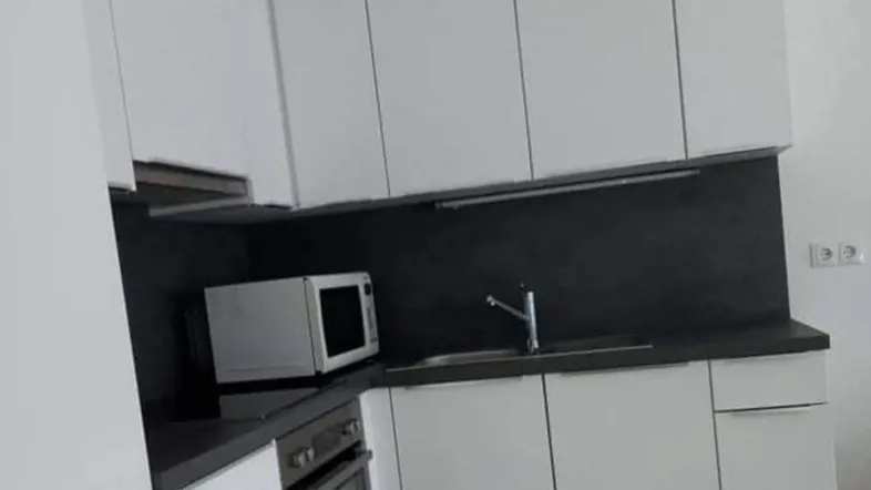 Moderne Einbauküche mit weißen Schränken, dunkler Arbeitsplatte und integrierten Geräten.