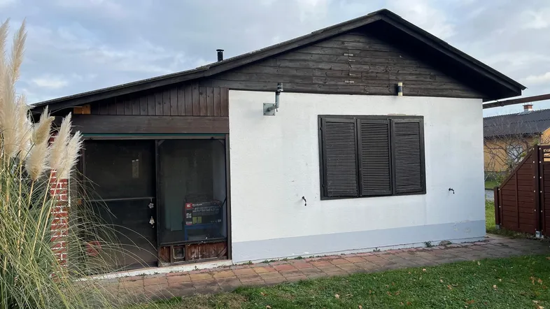 Kleines Haus mit weißer Fassade, Holzverkleidung und dunklen Fensterläden in ländlicher Umgebung.