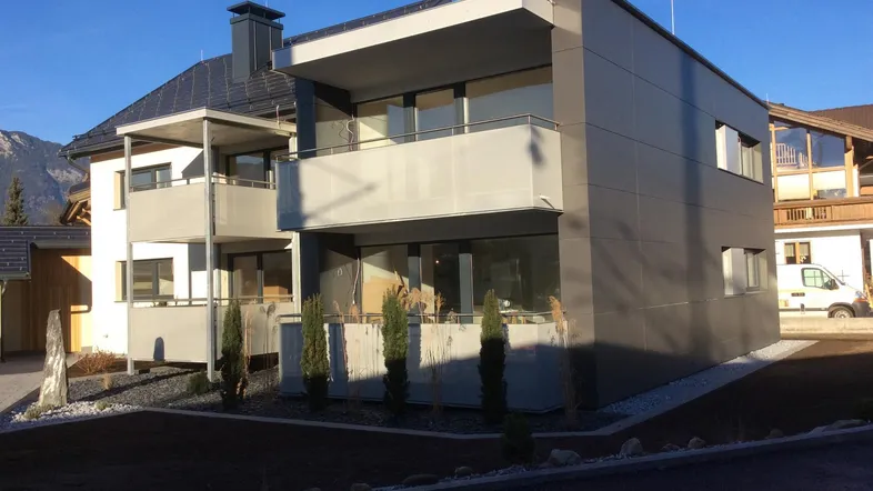 Modernes Mehrfamilienhaus mit Balkonen und dunkler Fassade in sonniger Lage.