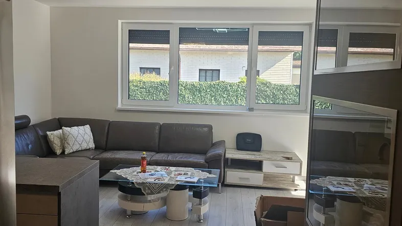 Helles Wohnzimmer mit modernem Ecksofa, Couchtisch und Blick ins Grüne durch große Fenster.