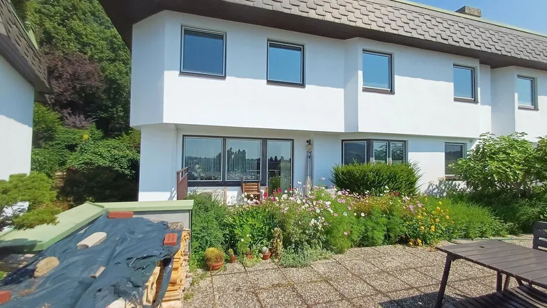 Große gepflasterte Terrasse mit Gartenbereich und Sitzgelegenheiten vor einem weißen Gebäude.