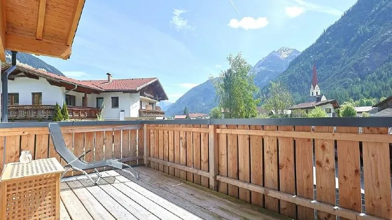 Geräumiger Holzbalkon mit Liegestuhl und atemberaubendem Blick auf die umliegenden Berge und das Tal.