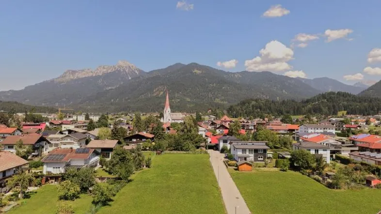 Luftaufnahme einer malerischen Stadt mit Bergen im Hintergrund und grünen Wiesen im Vordergrund.
