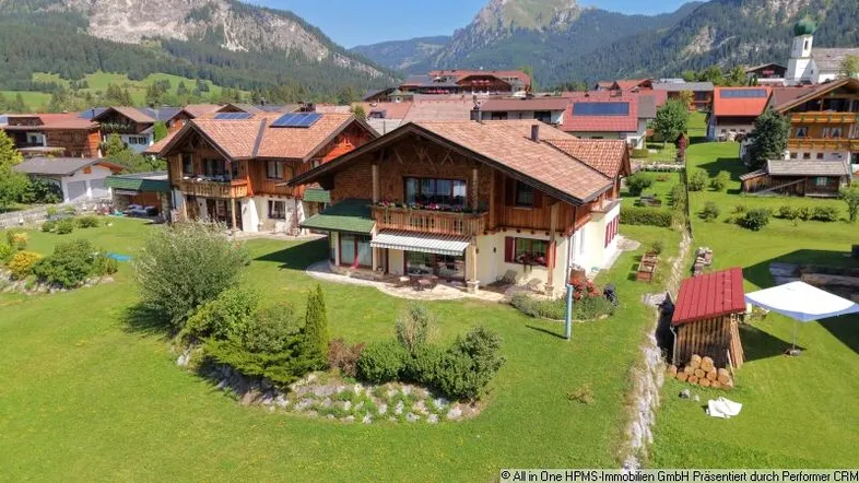Luftaufnahme eines charmanten Hauses im alpenländischen Stil mit Bergblick und gepflegtem Garten.