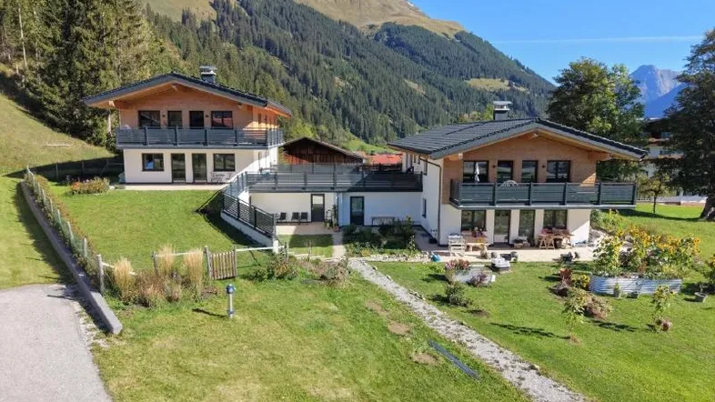 Zwei charmante Chalet-Häuser mit Balkonen und gepflegtem Garten vor beeindruckender Bergkulisse.