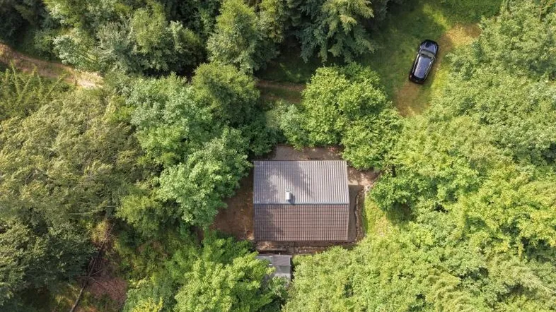 Luftaufnahme einer abgelegenen Holzhütte, umgeben von dichtem Wald und Natur.