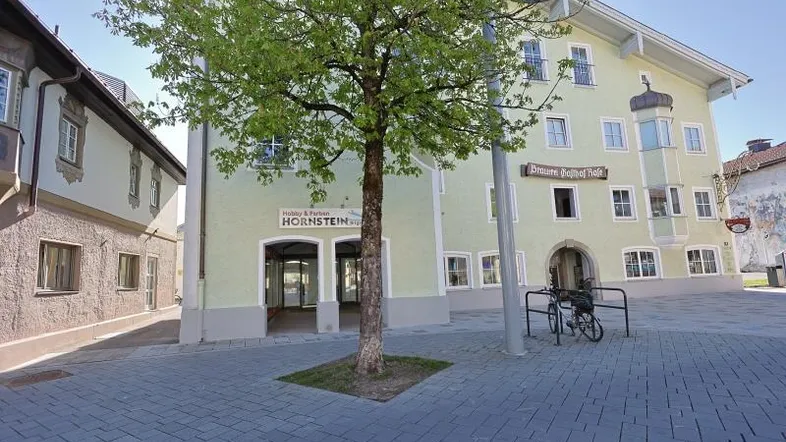 Historisches Gebäude mit hellgrüner Fassade und Geschäftsräumen im Erdgeschoss an einem sonnigen Tag.
