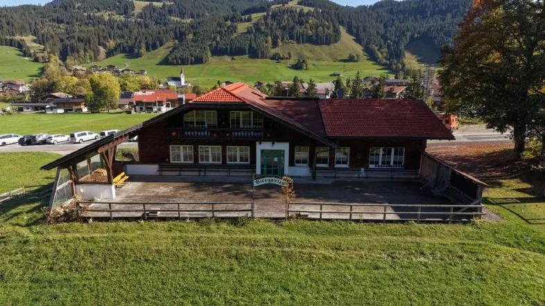 Luftaufnahme eines traditionellen Gebäudes mit rotem Dach und weitläufiger Grünfläche in den Bergen.