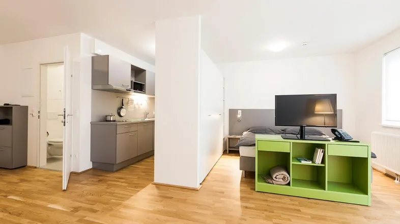 Helles Studio-Apartment mit integrierter Küchenzeile, Schlafbereich und modernem Holzfußboden.