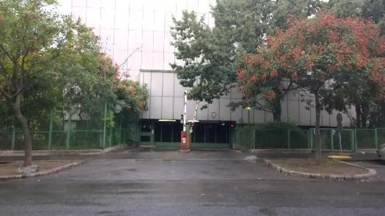 Einfahrt zu einer Tiefgarage mit Schranke, umgeben von Bäumen und einem Zaun.