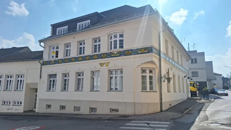Helles Eckgebäude mit traditioneller Architektur und dekorativen Elementen an einer sonnigen Straße, gut gepflegt.